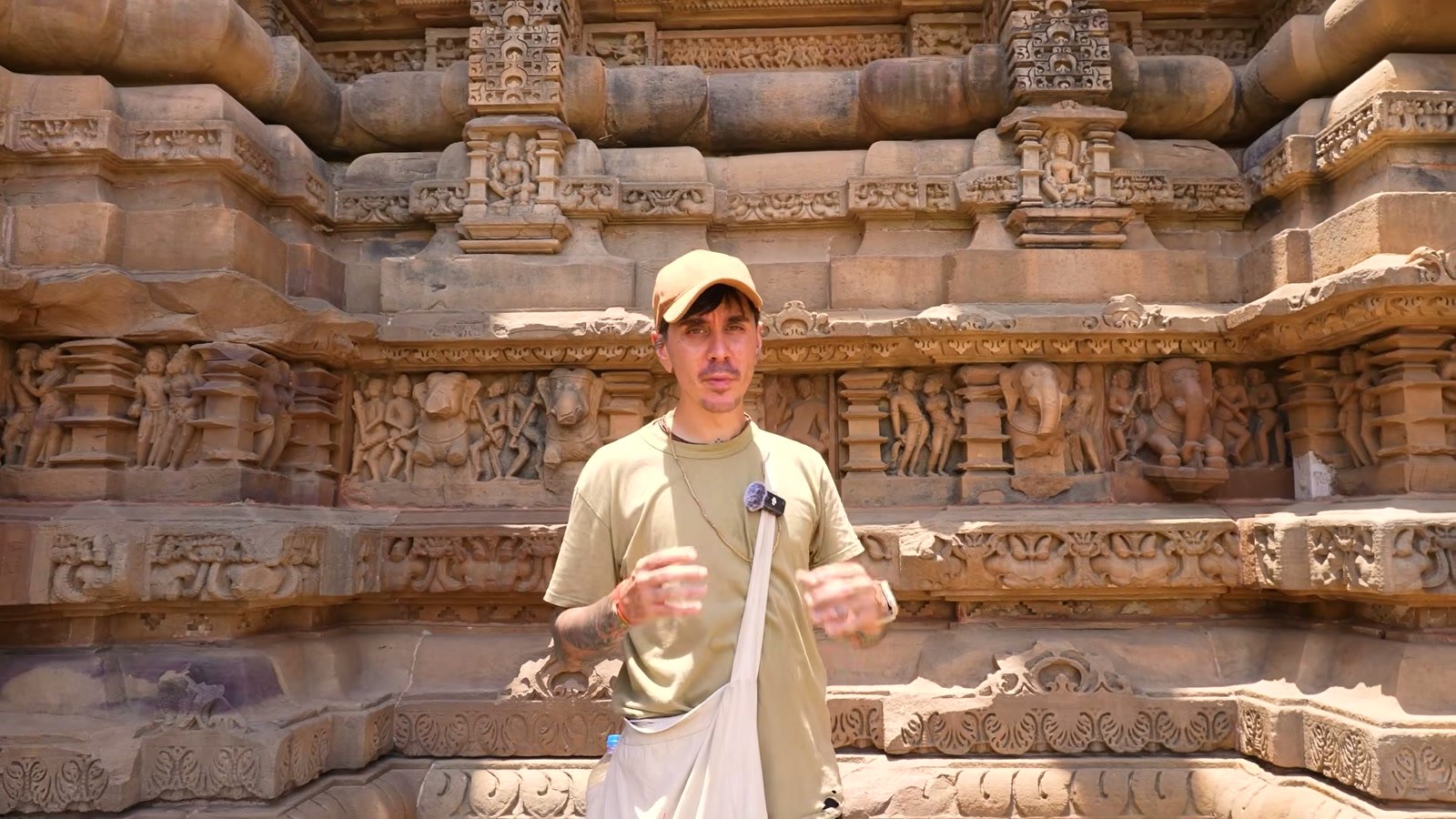 A traveller stands before an intricately carved sandstone temple wall covered in figures, in central India.
