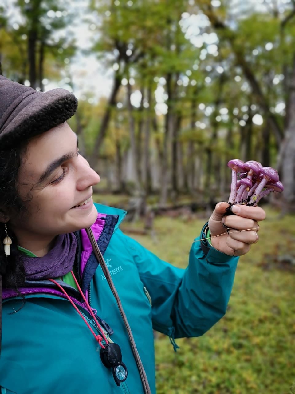 The mycologist Giuliana Furci smiling in the field, holding a cluster of purple mushrooms.