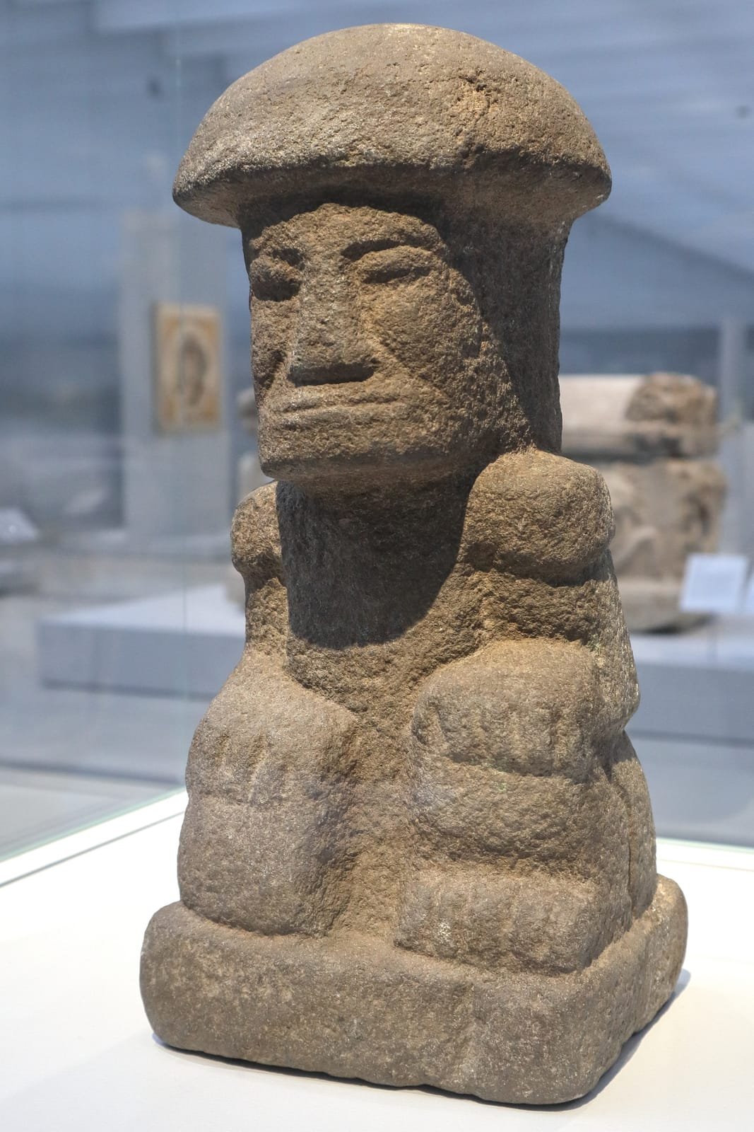 A carved Maya mushroom stone: a domed mushroom cap rising over a seated human figure, in grey volcanic stone.