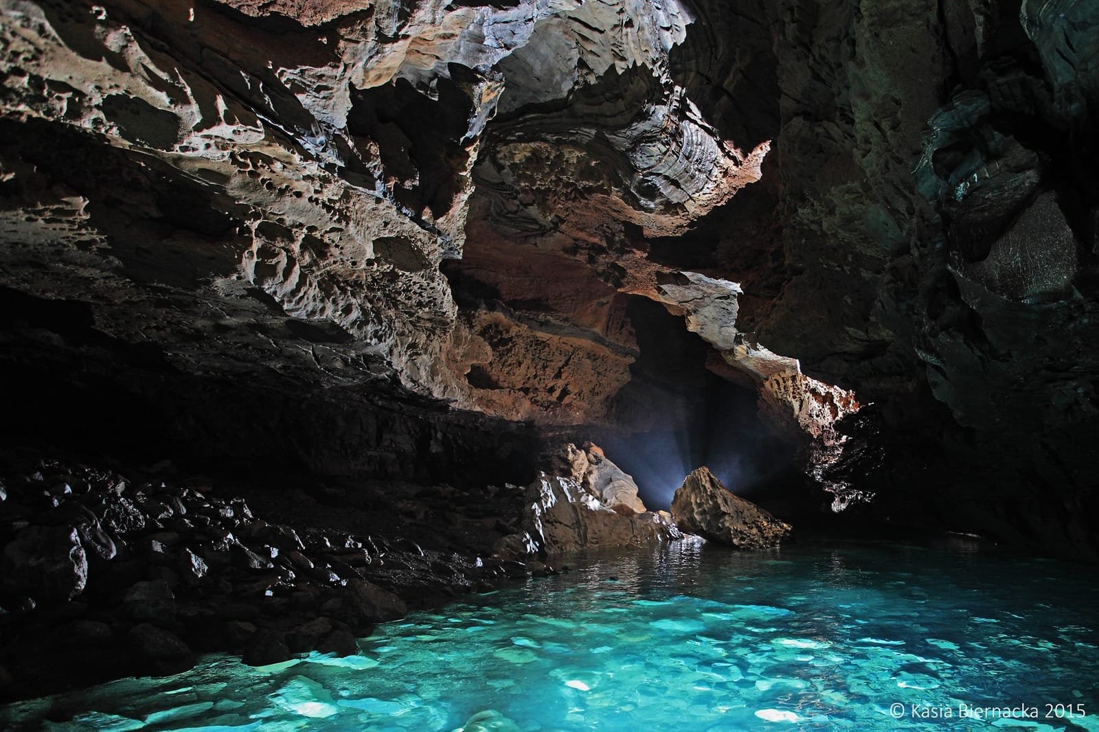 A glowing turquoise pool inside a vast cave chamber in the Sierra Mazateca, lit by a shaft of daylight.